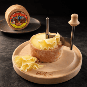 Tête de Moine AOP Swiss cheese on a wooden Girolle, with delicate cheese rosettes against a dark background.
