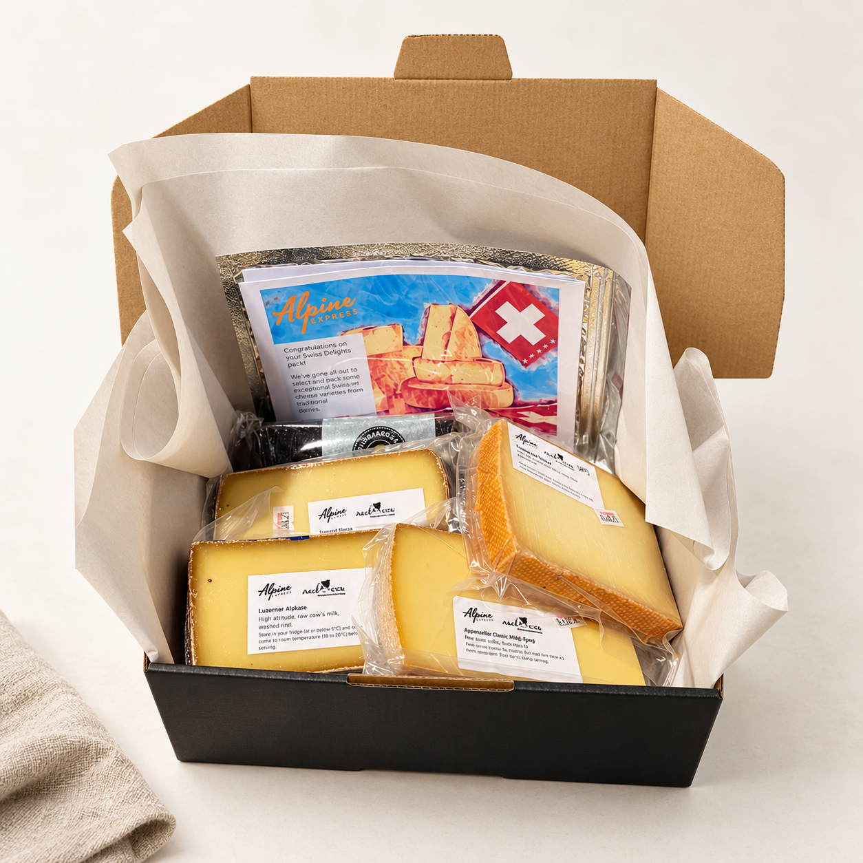 Open Alpine Express Swiss Delights sample box showing four wrapped cheese portions, packing tissue and an illustrated leaflet.